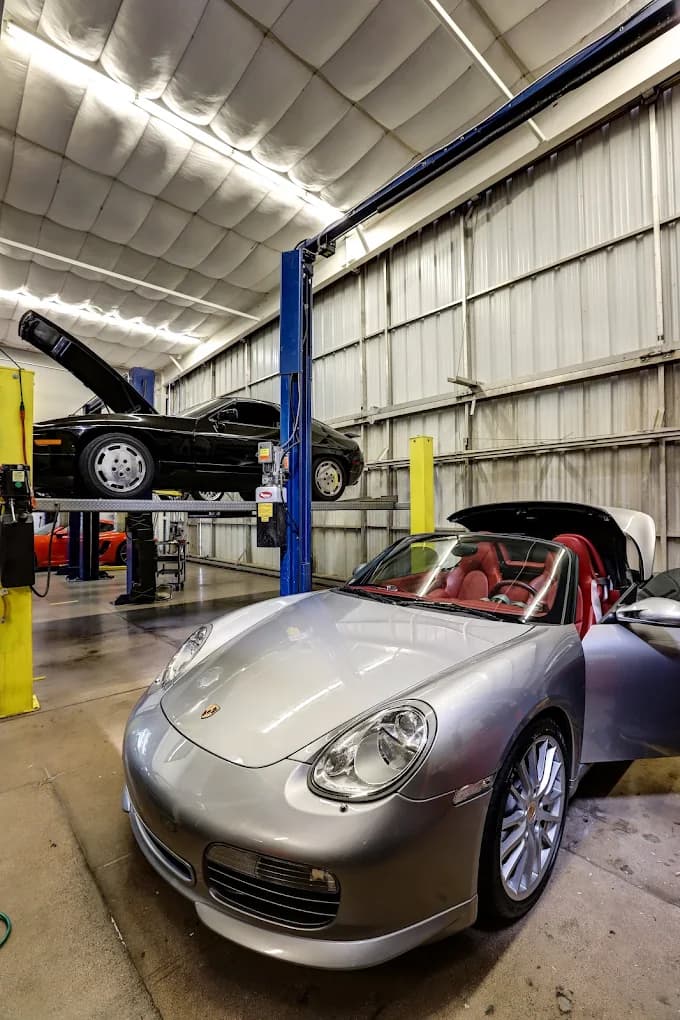 A silver Porsche 911 Cabriolet in the Exotic Motorwerks bay, a 928 up on the lift behind it.